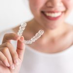 A Smiling Woman Holding Invisalign Or Invisible Braces, Orthodon