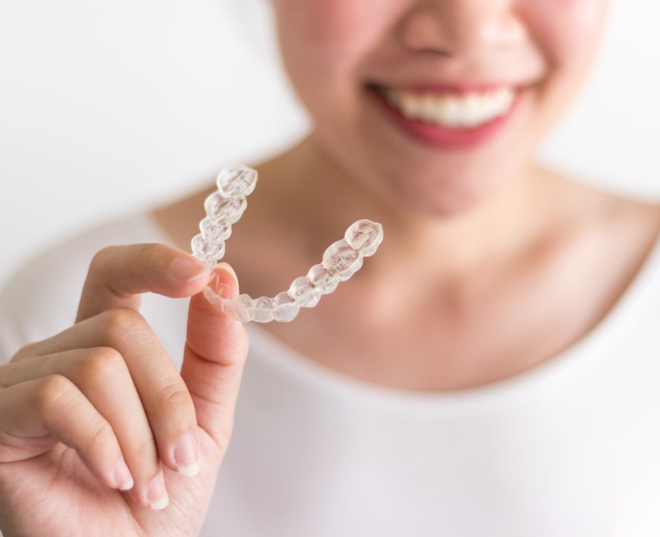 A Smiling Woman Holding Invisalign Or Invisible Braces, Orthodon
